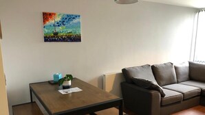 Un salon moderne avec une table à manger en bois, un canapé gris et un tableau coloré accroché au mur.