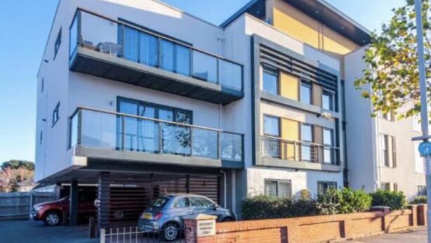 Un bâtiment moderne à deux étages, doté d’un garage et d’une voiture garée devant.