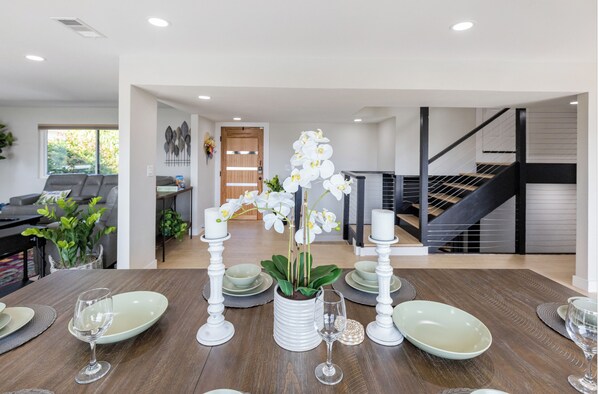 A dining area with a wooden table set for four, surrounded by white candles and a potted orchid.