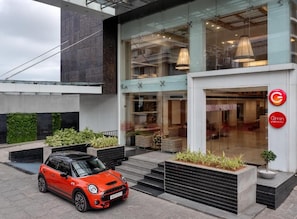 A modern building with a glass facade, a red car parked in front, and a sign with a red 'C' logo.