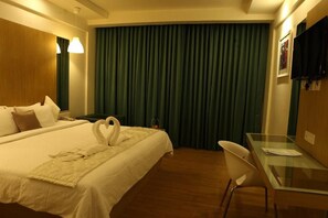 A hotel room with a bed, a desk, a chair, a television, and a curtain.