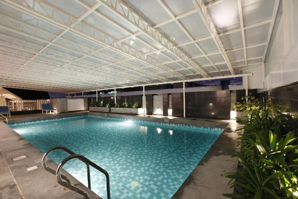 An indoor swimming pool with a tiled floor, a metal pool ladder, and a glass ceiling structure.