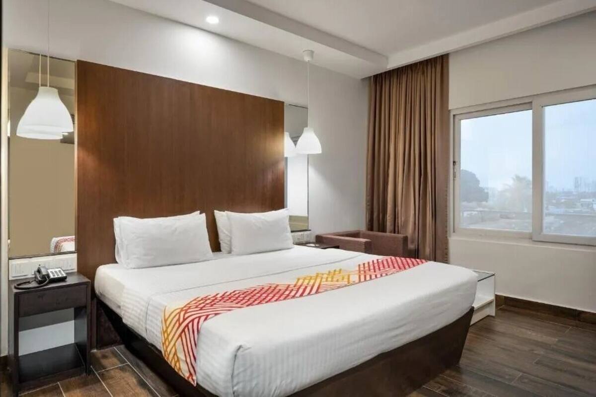 Ein modernes Hotelzimmer mit einem großen Bett, Nachttischen, einem Schreibtisch und einem großen Fenster mit Blick auf die Stadt.