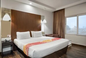 Une chambre d’hôtel moderne dotée d’un grand lit, de tables de chevet, d’un bureau et d’une grande fenêtre donnant sur la ville.