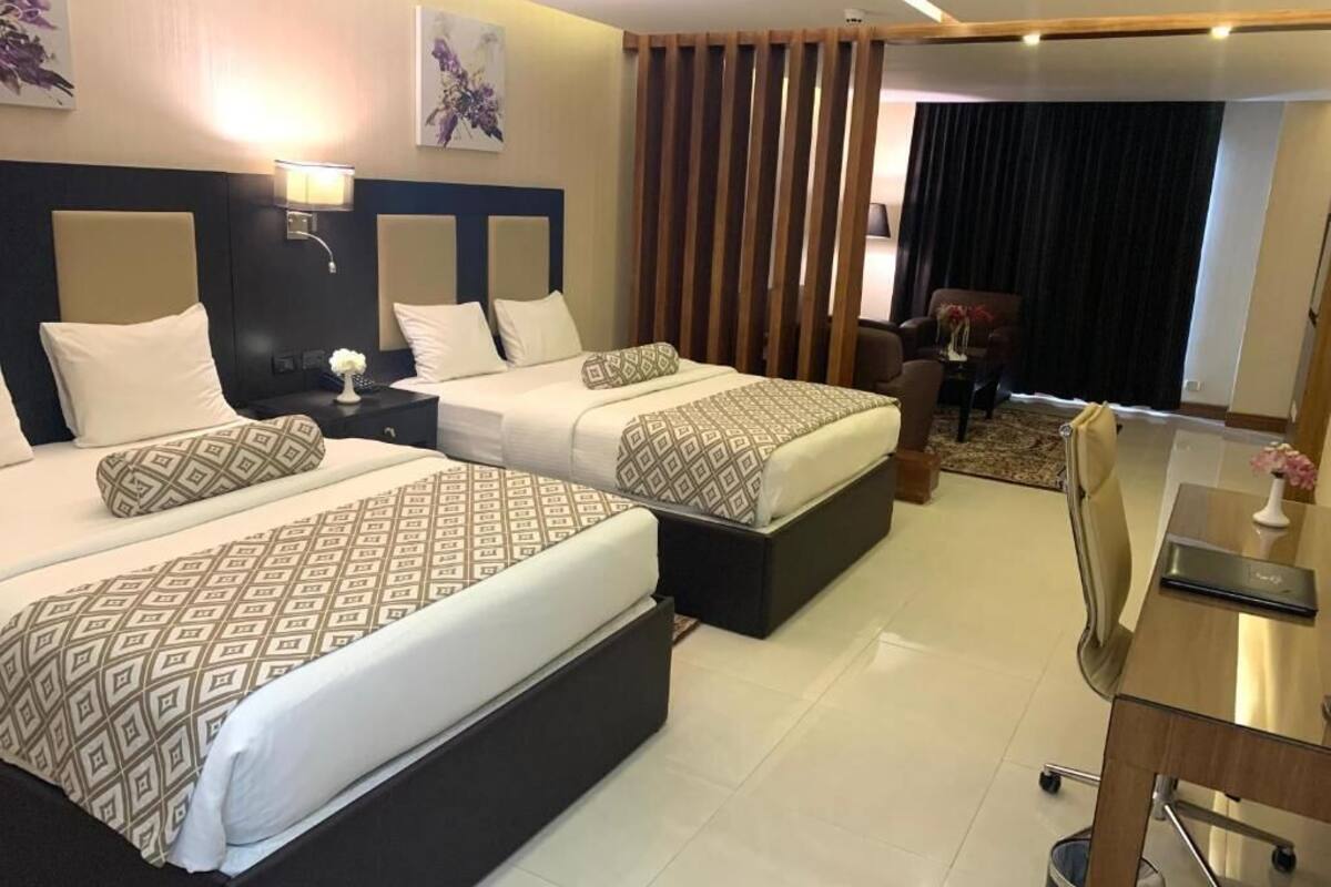 A hotel room with two beds, a desk, a chair, and a small table with a vase.
