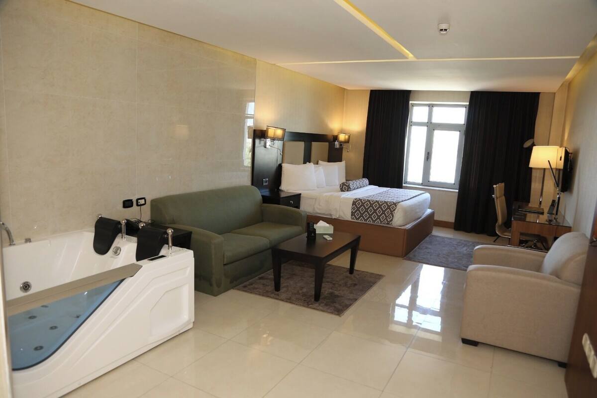 A hotel room with a bed, a sofa, a desk, a chair, a TV, and a bathtub.