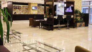 A hotel reception area with a reception desk, seating area, and a television screen displaying a cityscape.