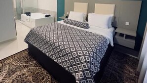 A modern bedroom with a large bed, a bedside table, a nightstand, a mirror, and a shower area.