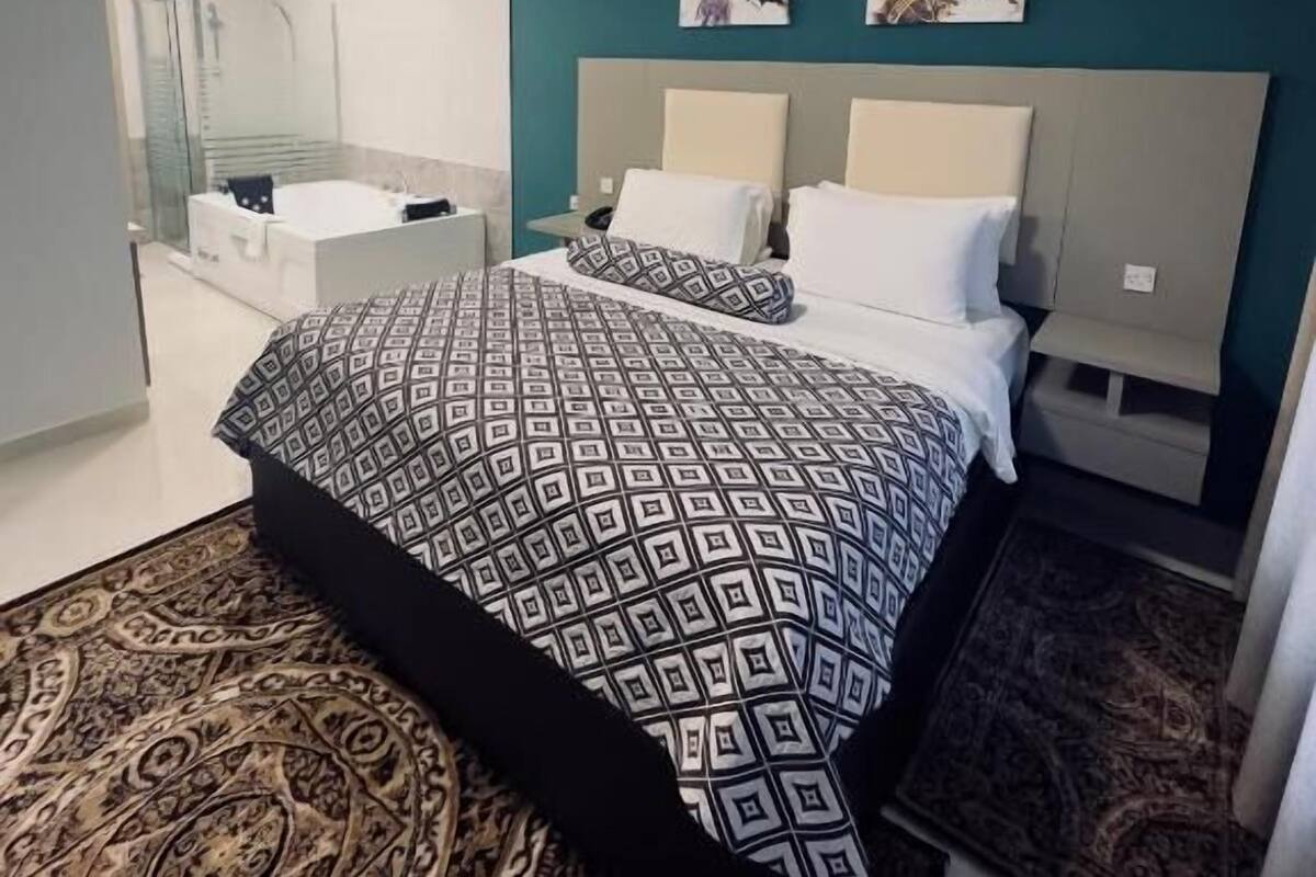 A modern bedroom with a large bed, a bedside table, a nightstand, a mirror, and a shower area.