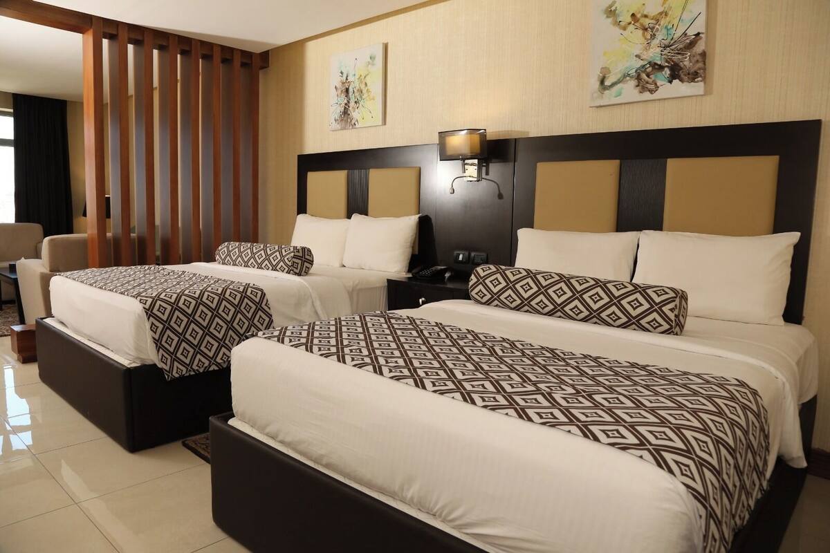 A hotel room with two beds, a nightstand, a lamp, and artwork on the walls.