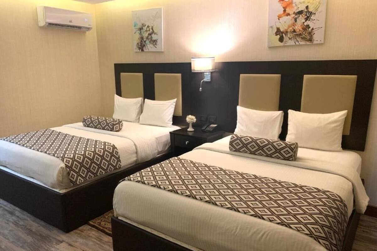 Two adjacent beds with patterned bedding, a nightstand with a lamp, and artwork on the walls.