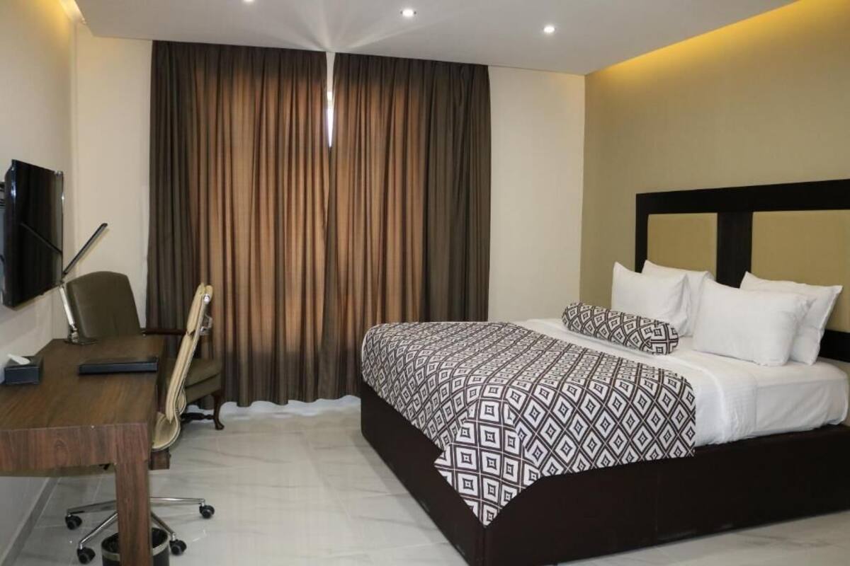 A hotel room with a large bed, a desk with a chair, a television, and a curtain.