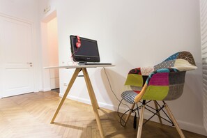 A laptop on a wooden stand, a colorful chair, and a white door in a room with wooden flooring.