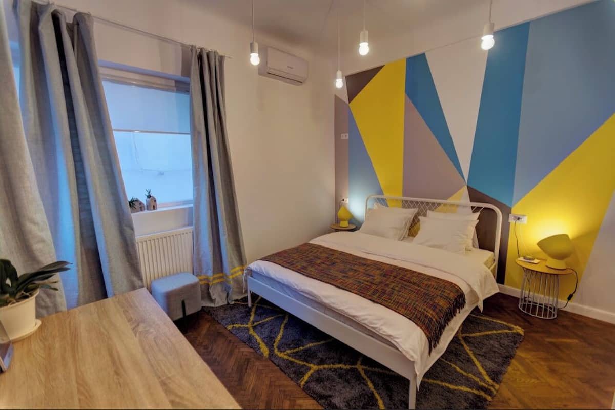 A modern bedroom with a bed, a bedside table, a potted plant, a radiator, and a window with curtains.