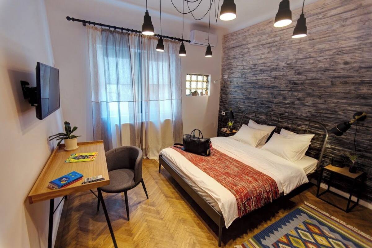 A modern bedroom with a bed, desk, chair, and a TV.