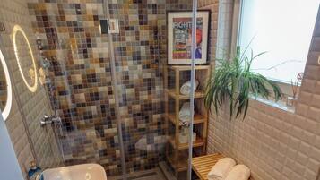 Un baño moderno con cabina de ducha de vidrio, un lavamanos, un inodoro y un banco de madera con toallas.