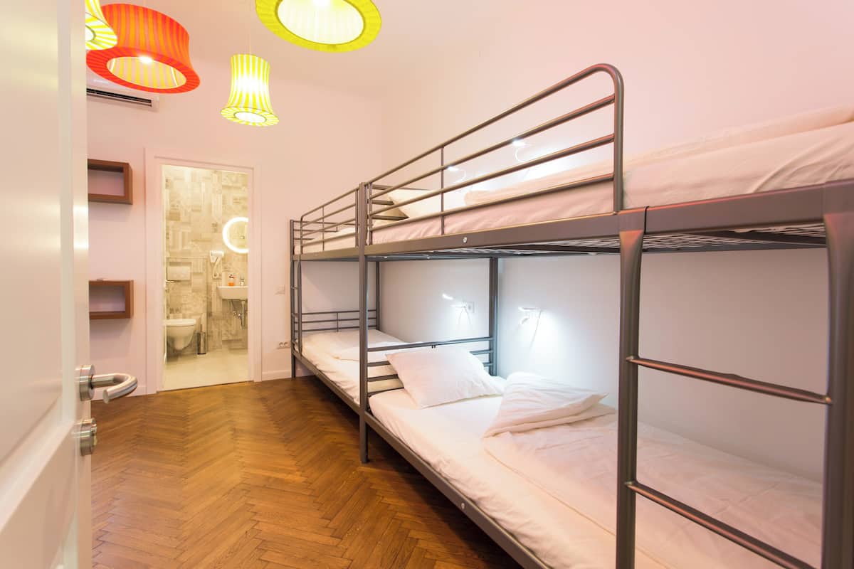 A bunk bed room with a wooden floor, a bathroom with a sink and mirror, and a door leading to another room.
