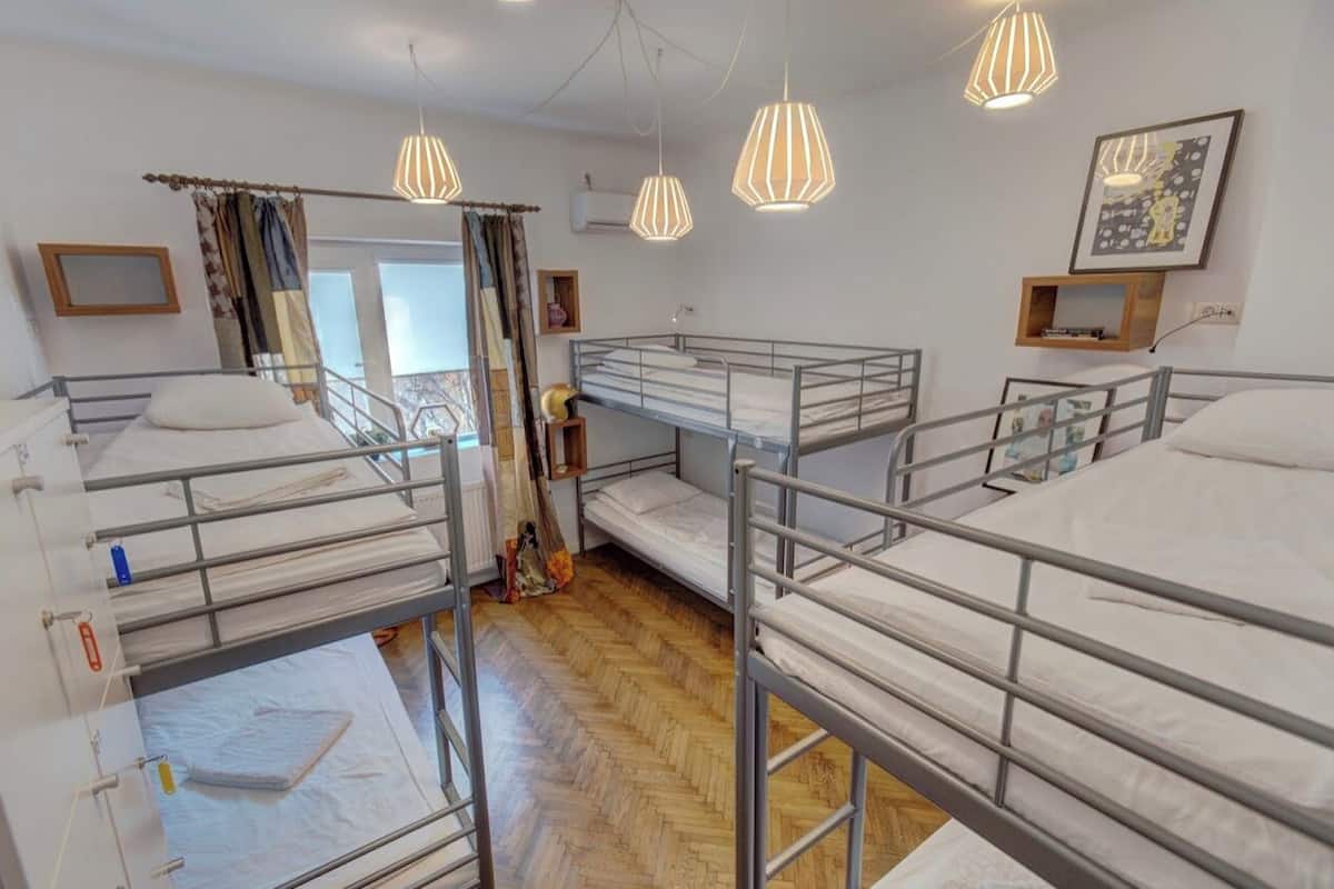 A dormitory room with bunk beds, a wooden floor, and pendant lights.