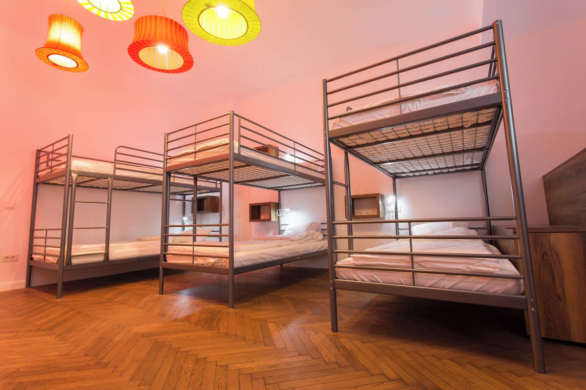 A room with bunk beds, wooden flooring, and three hanging lamps.