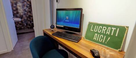 Una oficina pequeña con una computadora de escritorio, un teclado, un ratón y un cartel que dice "LUCRATI AICI!".