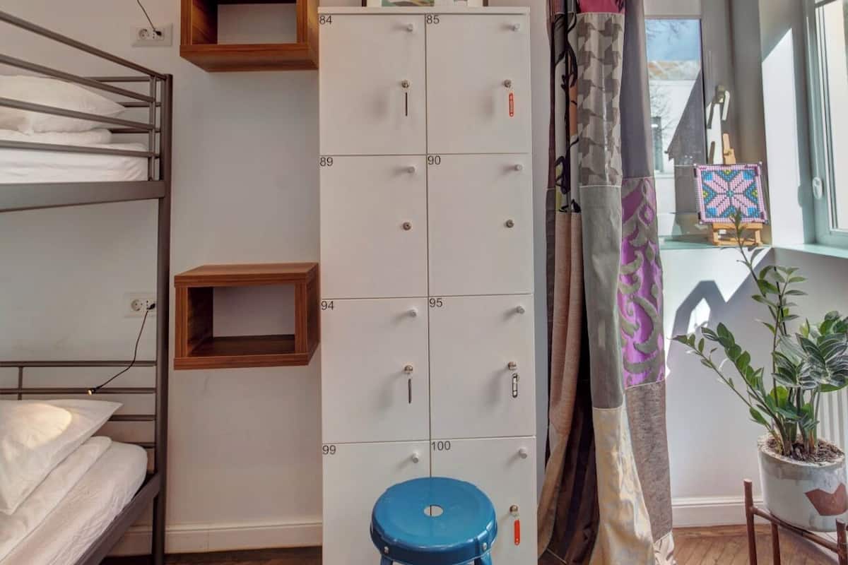 A dormitory room with bunk beds, a wardrobe, a stool, and a window with a view.