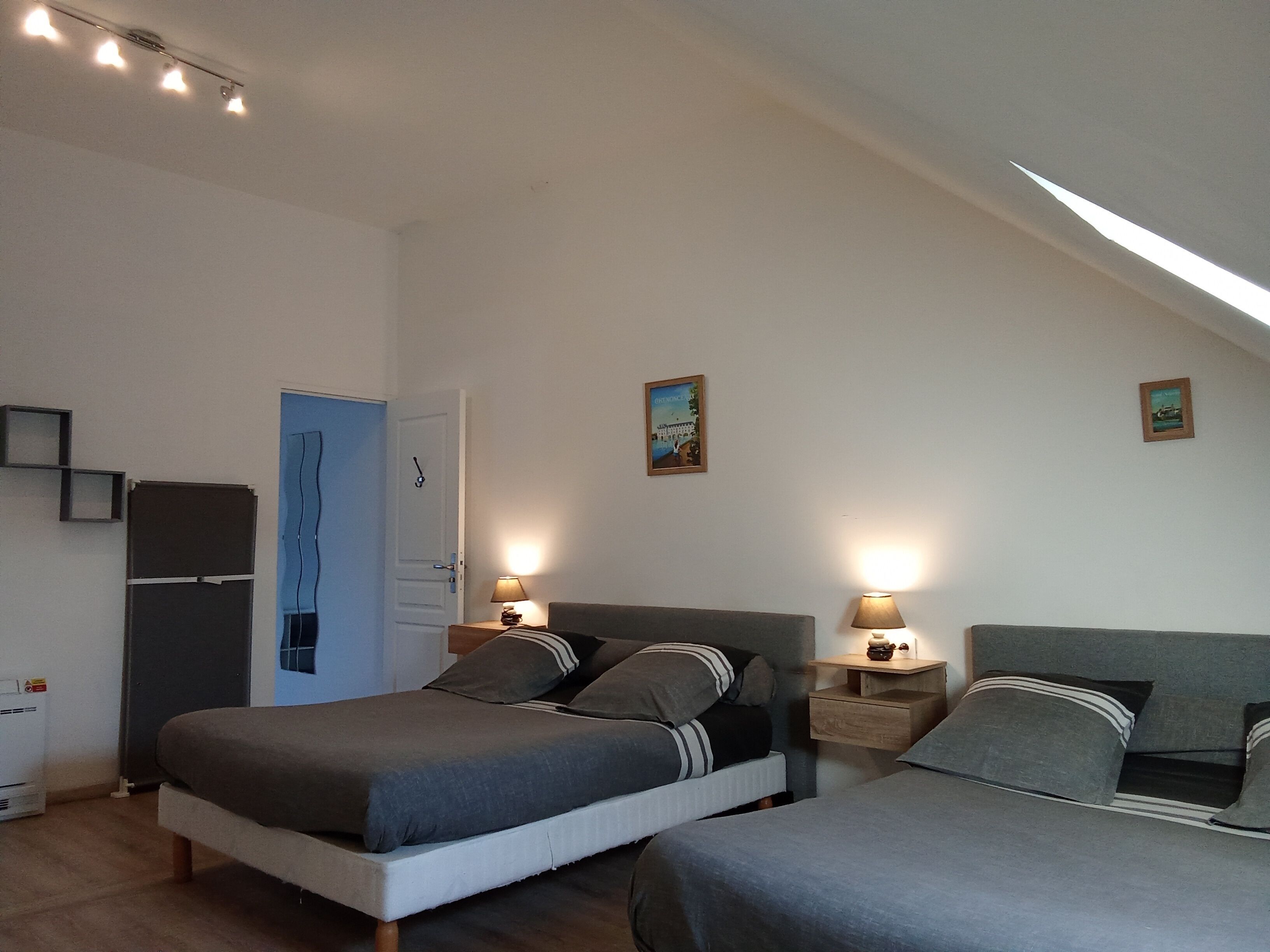 A bedroom with two beds, a wardrobe, a door, and a small table with a lamp.