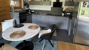 Una cocina moderna con armarios grises, un refrigerador de acero inoxidable y un comedor con una mesa redonda y sillas negras.