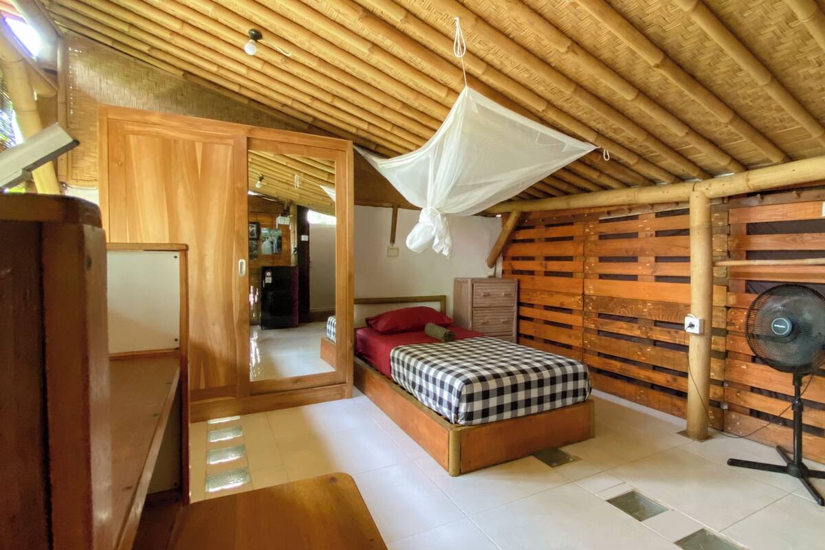 Una habitación con una cama, un ventilador, un armario de madera y una mosquitera.
