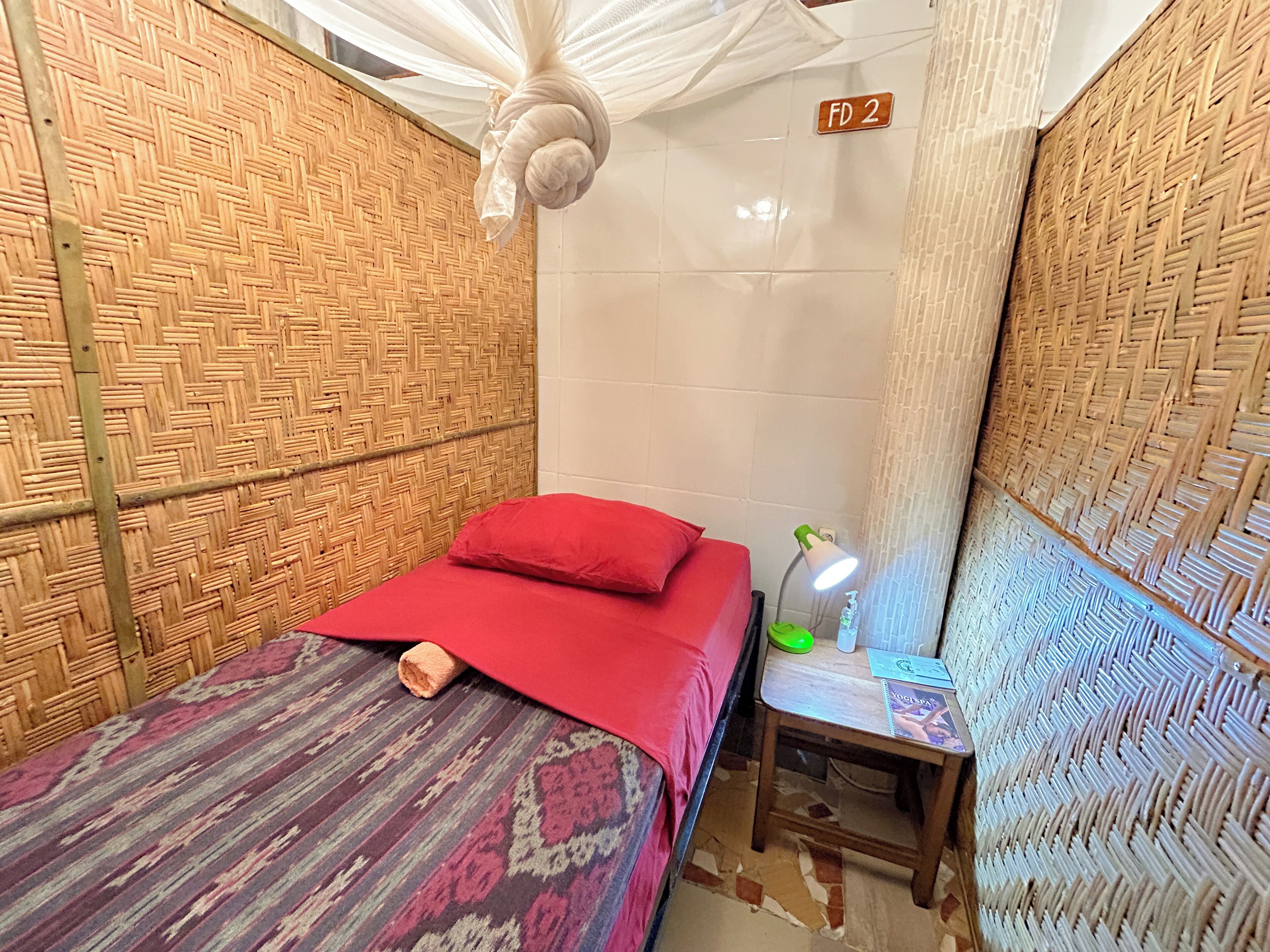 A room with a bed, a nightstand, a lamp, and a woven wall.