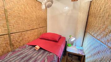 Een kamer met een bed, nachtkastje, lamp en wandkleed.