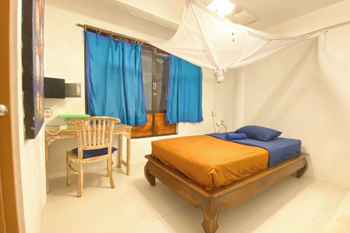 Un dormitorio con cama de madera, cortinas azules, una silla de madera y un escritorio.