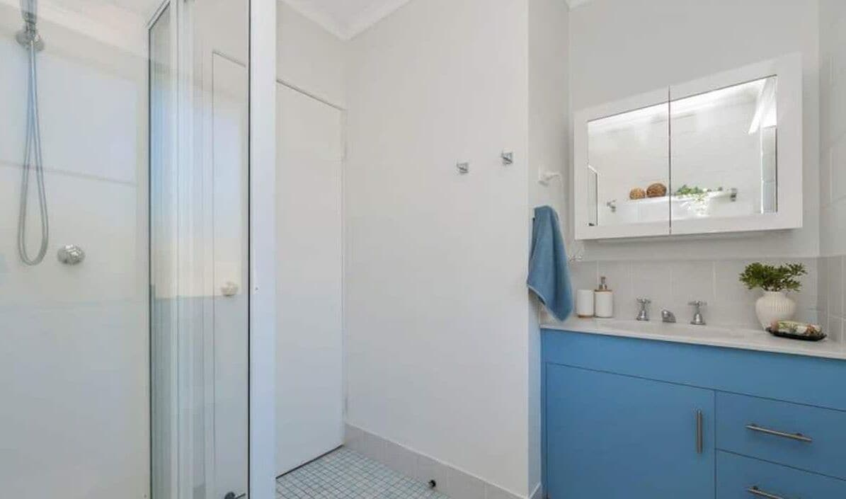 Un bagno con box doccia in vetro, un mobile lavabo bianco con armadietto blu e uno specchio sopra il lavandino.