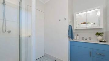 Un bagno con box doccia in vetro, un mobile lavabo bianco con armadietto blu e uno specchio sopra il lavandino.