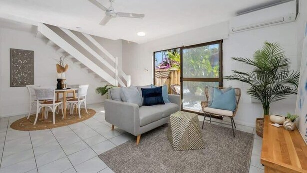 A modern living room with a grey sofa, white chairs, a wooden coffee table, and a large window with a view of greenery.