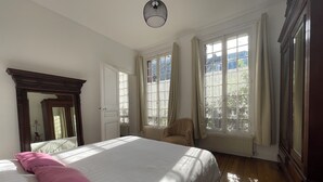A bedroom with a large bed, a chair, a window, and a mirror. - Maison au Calme et au Vert au Cœur du Centre Ville (Vincennes)