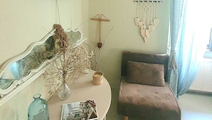 A living room with a flat-screen TV mounted on the wall, an air conditioning unit, a small table with a vase and a magazine, a couch, and a decorative hanging piece.