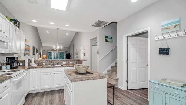 A modern kitchen with white cabinets, a central island, and a staircase leading to another level. - TB 93C Wonderful 3/bed 2/bath Garden home in True Blue (Pawleys Island)