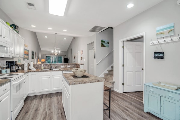 A modern kitchen with white cabinets, a central island, and a staircase leading to another level.