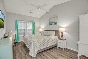 A bedroom with a bed, bedside lamps, a ceiling fan, a window with curtains, and a painting on the wall.