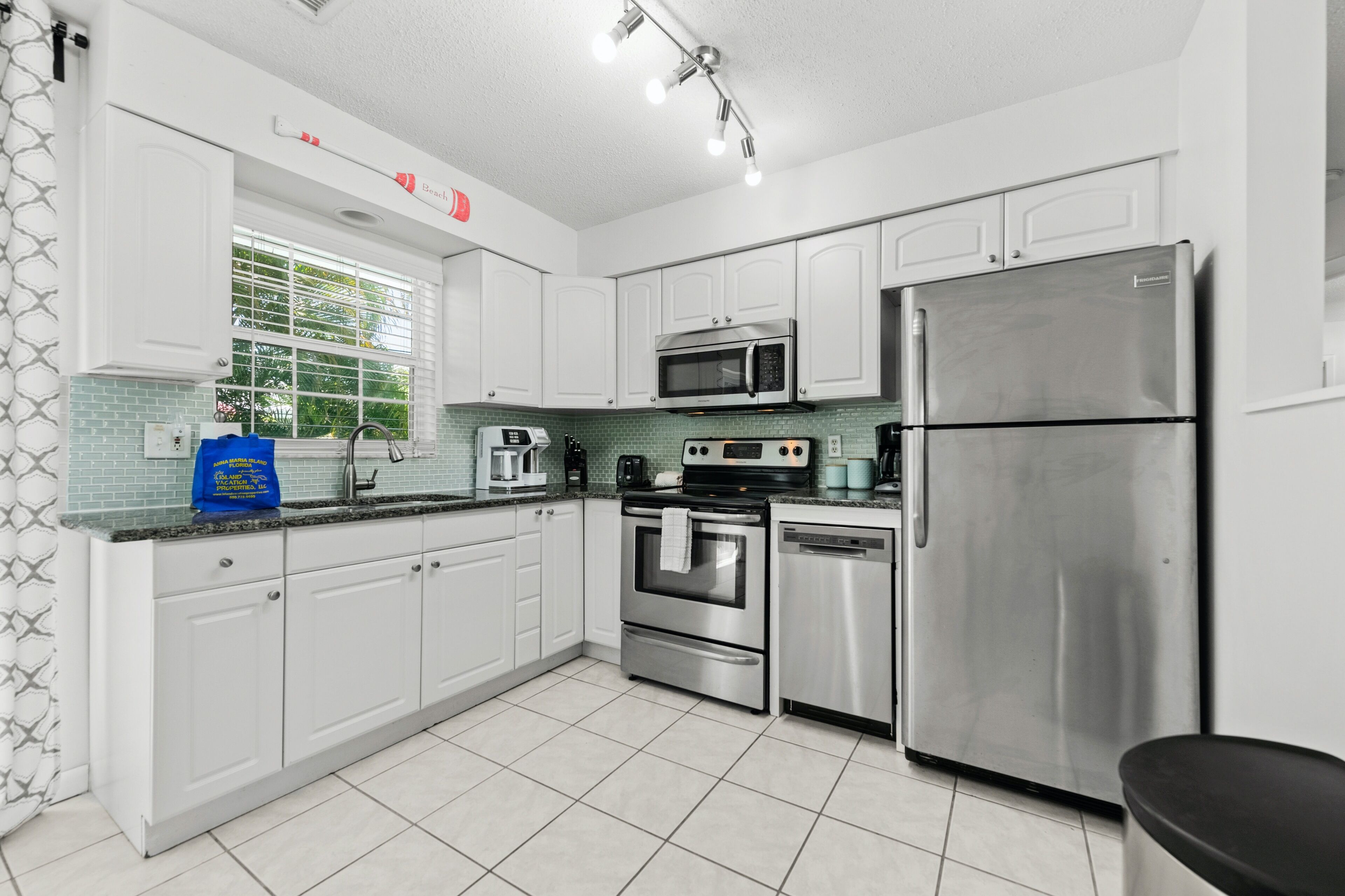 A modern kitchen with white cabinets, stainless steel appliances, and a window with blinds.
