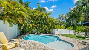 A backyard with a swimming pool, brick patio, and yellow Adirondack chairs.