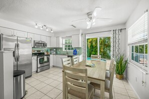 Een moderne keuken met roestvrijstalen apparatuur, een eethoek met tafel en stoelen, en uitzicht op een zwembad door grote ramen.