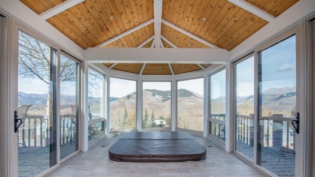 A spacious room with a wooden ceiling, large windows, and a view of mountains. - Spacious Mountain Manor with 9 bedrooms, 11 baths and Hot Tub (Crested Butte)