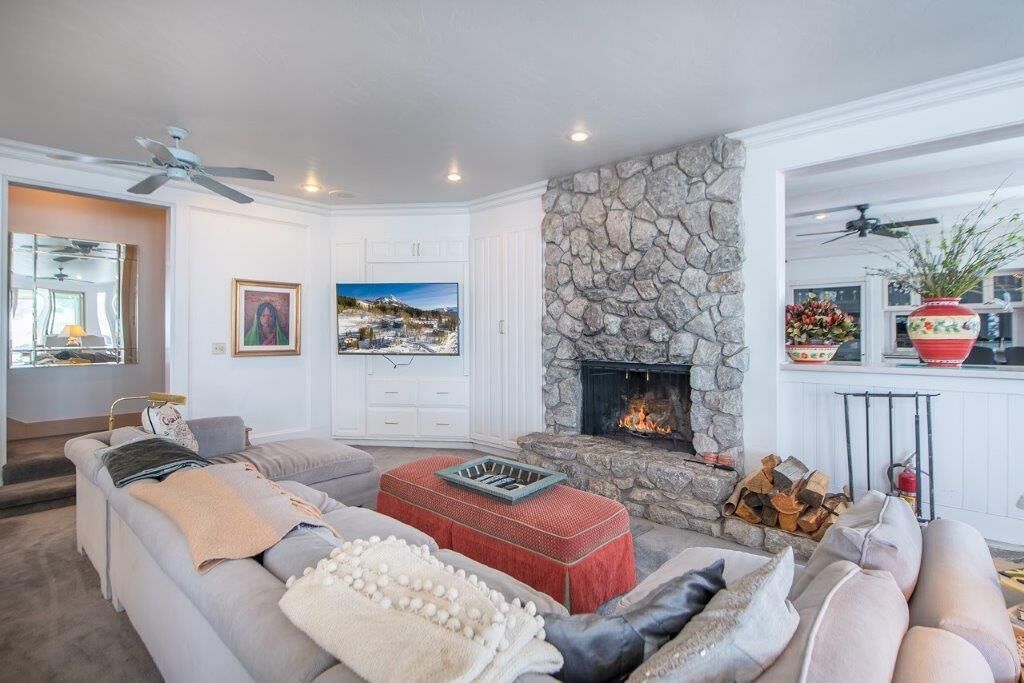 A living room with a stone fireplace, a large window with a cityscape view, and a cozy seating area with a sofa and ottoman.