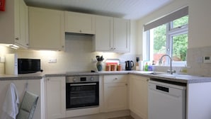 A kitchen with white cabinets, a microwave, an oven, a dishwasher, and a window with a view of greenery.