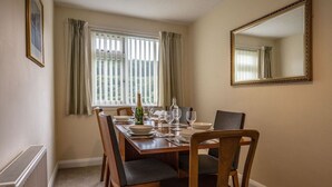 A dining room with a wooden table set for four, a radiator, a window with curtains, and a mirror on the wall.