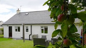 A white house with a grey roof, a front door, and a small porch with wicker furniture.