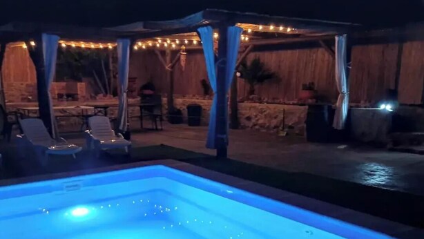 An outdoor swimming pool with a canopy and string lights, surrounded by lounge chairs and a rustic setting. - la Cordobesa (Priego de Córdoba)