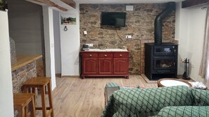 A cozy living room with a stone wall, a fireplace, a television mounted on the wall, and wooden furniture. - la Cordobesa (Priego de Córdoba)
