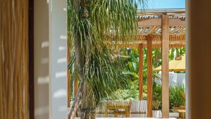 A modern outdoor patio area with a wooden pergola, a palm tree, and various plants. - Villa Air - 2BR Villa in Pererenan (Canggu)